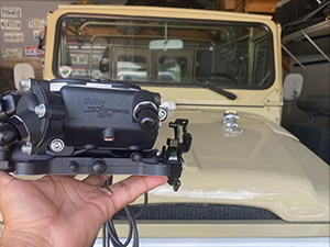 Hand holding fuel injection upgrade in front of a Toyota Land Cruiser FJ40